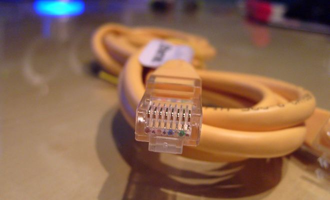 Primer plano de un conector RJ45 de un cable Ethernet amarillo enrollado sobre una mesa.