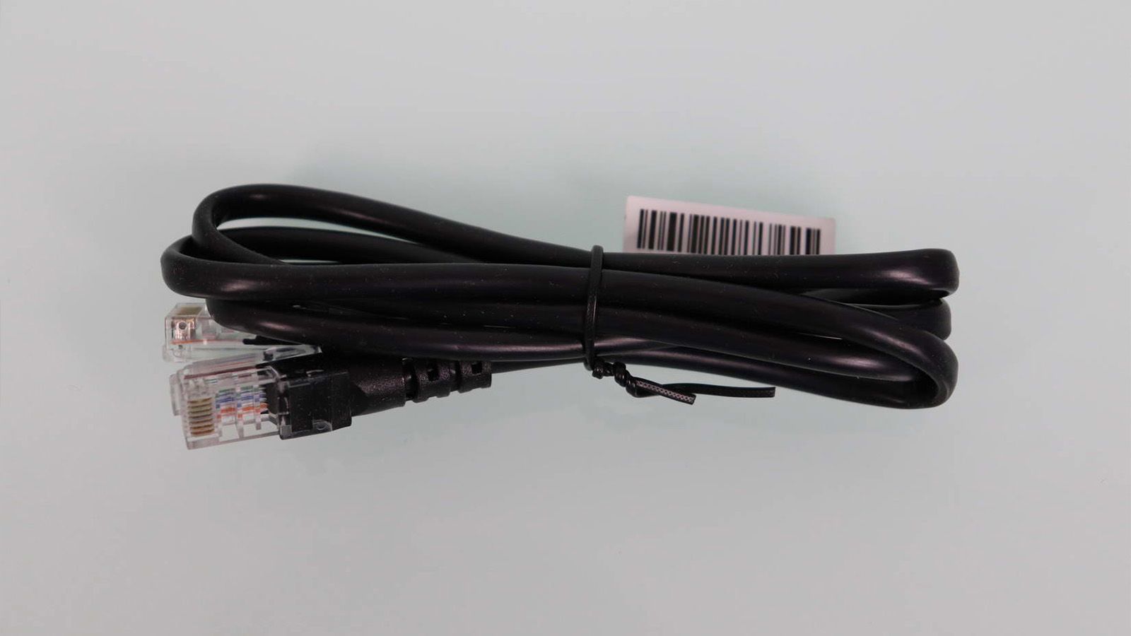Cable Ethernet negro enrollado con conectores RJ45 y etiqueta de código de barras sobre un fondo claro.