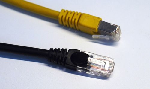 Primer plano de conectores RJ45 de dos cables Ethernet en color amarillo y negro sobre fondo blanco.