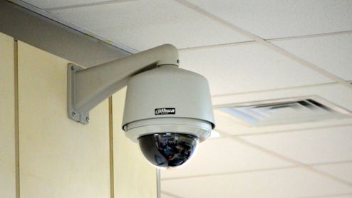 Cámara de seguridad tipo domo instalada en el soporte de una pared interior cerca del techo.