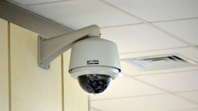 Cámara de seguridad tipo domo instalada en el soporte de una pared interior cerca del techo.