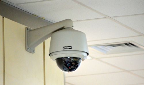 Cámara de seguridad tipo domo instalada en el soporte de una pared interior cerca del techo.