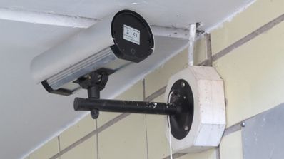 Cámara de vigilancia tipo bala instalada con un soporte de brazo largo en una pared exterior de azulejos.