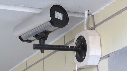 Cámara de vigilancia tipo bala instalada con un soporte de brazo largo en una pared exterior de azulejos.
