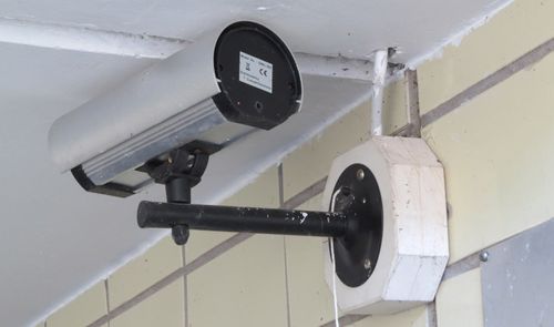 Cámara de vigilancia tipo bala instalada con un soporte de brazo largo en una pared exterior de azulejos.