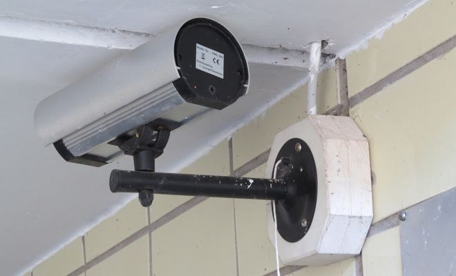 Cámara de vigilancia tipo bala instalada con un soporte de brazo largo en una pared exterior de azulejos.