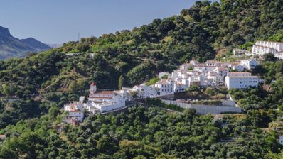Vista panorámica de un pueblo de casas blancas ubicado en la ladera de una montaña boscosa bajo un cielo despejado.