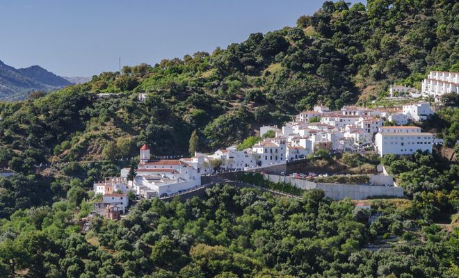 Vista panorámica de un pueblo de casas blancas ubicado en la ladera de una montaña boscosa bajo un cielo despejado.