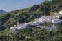 Vista panorámica de un pueblo de casas blancas ubicado en la ladera de una montaña boscosa bajo un cielo despejado.