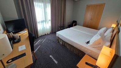 Habitación de hotel con dos camas individuales unidas, escritorio con televisor y armario de madera en Ciudad Real.