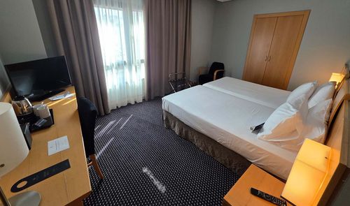 Habitación de hotel con dos camas individuales unidas, escritorio con televisor y armario de madera en Ciudad Real.