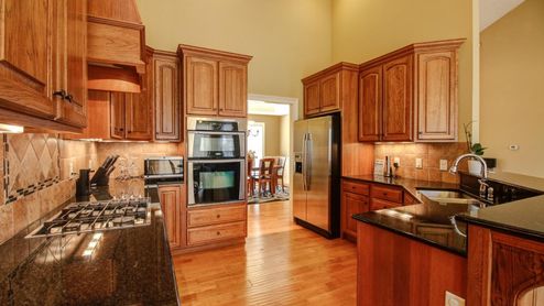 Cocina con muebles de madera, encimera de granito oscuro y electrodomésticos de acero inoxidable encastrados.