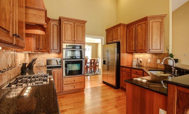 Cocina con muebles de madera, encimera de granito oscuro y electrodomésticos de acero inoxidable encastrados.