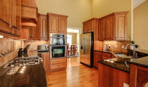 Cocina con muebles de madera, encimera de granito oscuro y electrodomésticos de acero inoxidable encastrados.