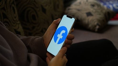 Persona sosteniendo un teléfono móvil con el logotipo de Facebook en pantalla.