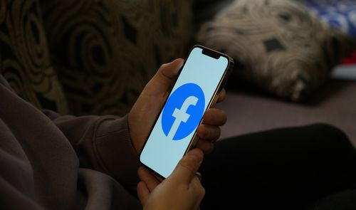 Persona sosteniendo un teléfono móvil con el logotipo de Facebook en pantalla.
