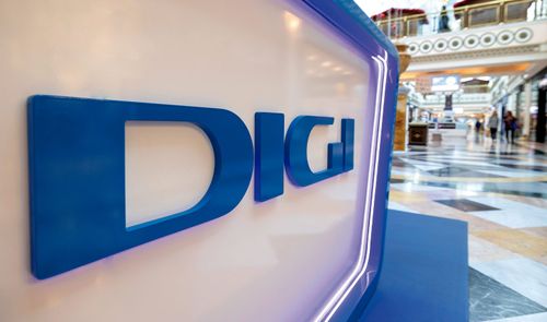 Logotipo de DIGI en letras azules corpóreas sobre un soporte blanco iluminado en un centro comercial.