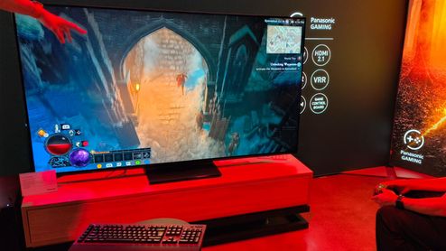 Televisor de gran formato mostrando una partida de videojuego de rol en un entorno de exposición con iluminación roja.