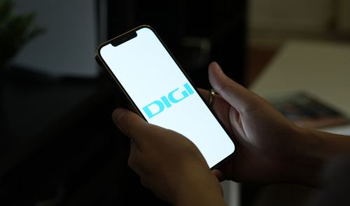Manos sujetando un teléfono móvil que muestra el logotipo de DIGI en pantalla sobre un fondo blanco.