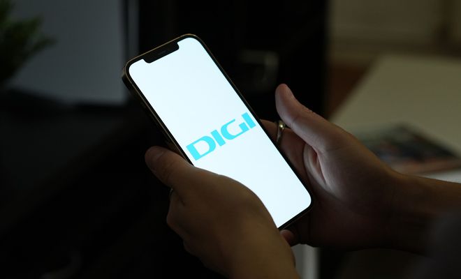 Manos sujetando un teléfono móvil que muestra el logotipo de DIGI en pantalla sobre un fondo blanco.