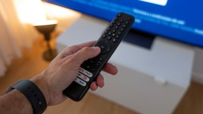 Primer plano de una mano sosteniendo un mando a distancia frente a una Smart TV con pantalla azul.