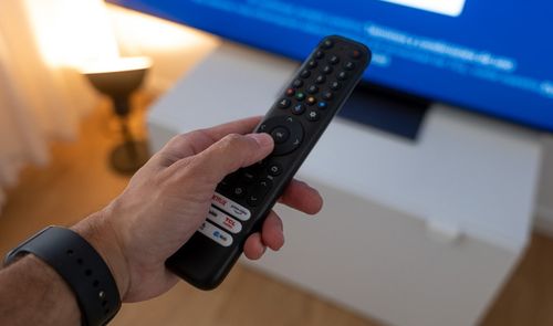 Primer plano de una mano sosteniendo un mando a distancia frente a una Smart TV con pantalla azul.