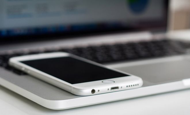Primer plano de un teléfono móvil blanco colocado sobre el reposamuñecas de un ordenador portátil.