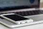 Primer plano de un teléfono móvil blanco colocado sobre el reposamuñecas de un ordenador portátil.