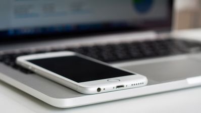 Primer plano de un teléfono móvil blanco colocado sobre el reposamuñecas de un ordenador portátil.