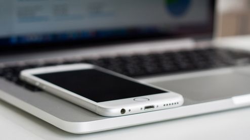 Primer plano de un teléfono móvil blanco colocado sobre el reposamuñecas de un ordenador portátil.