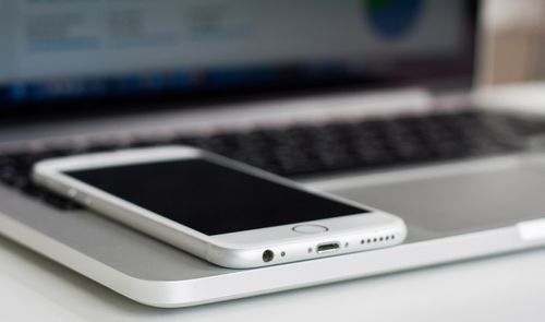 Primer plano de un teléfono móvil blanco colocado sobre el reposamuñecas de un ordenador portátil.