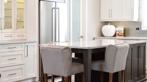 Cocina moderna con isla central oscura, sillas tapizadas en gris y armarios blancos.