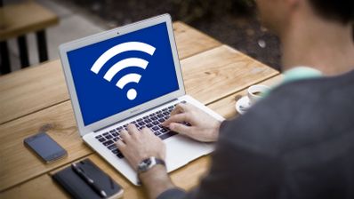 Persona utilizando un ordenador portátil en una mesa de madera con el símbolo de WiFi en pantalla.