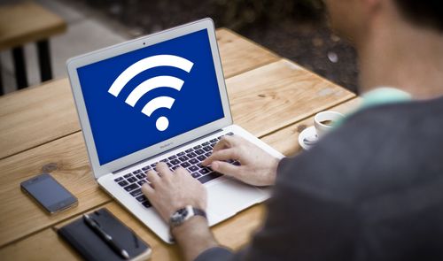 Persona utilizando un ordenador portátil en una mesa de madera con el símbolo de WiFi en pantalla.