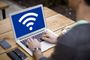 Persona utilizando un ordenador portátil en una mesa de madera con el símbolo de WiFi en pantalla.