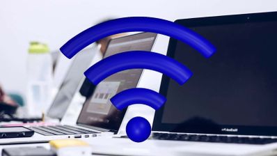 Icono de señal Wi-Fi en color azul superpuesto a varios ordenadores portátiles en una oficina.