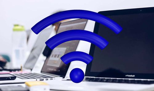Icono de señal Wi-Fi en color azul superpuesto a varios ordenadores portátiles en una oficina.