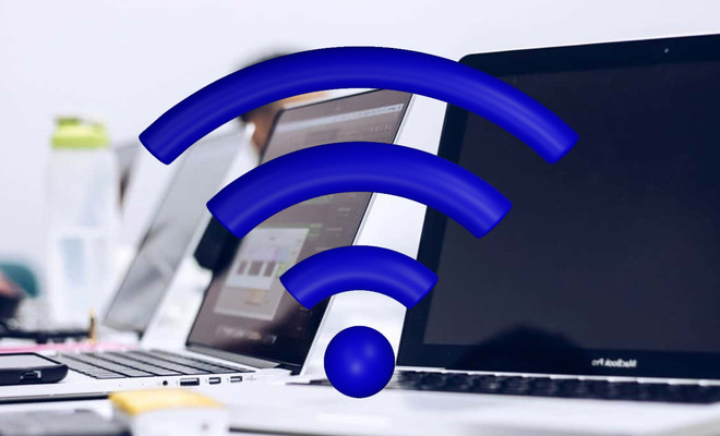 Icono de señal Wi-Fi en color azul superpuesto a varios ordenadores portátiles en una oficina.