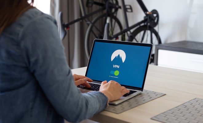 Persona sentada a la mesa trabajando con un ordenador portátil que muestra la interfaz de conexión de una VPN.