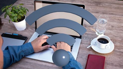 Persona trabajando con un ordenador portátil en una mesa de madera con un icono de señal Wi-Fi superpuesto.