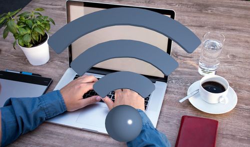 Persona trabajando con un ordenador portátil en una mesa de madera con un icono de señal Wi-Fi superpuesto.