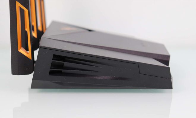 Vista lateral de un router ASUS TUF-AX4200 de color negro con rejillas de ventilación y antenas con detalles en naranja.