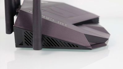 Vista lateral del router TUF-AX6000 con rejillas de ventilación y antenas externas en color oscuro.