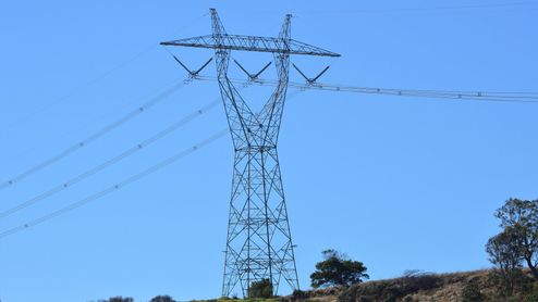 Torre de alta tensión de estructura metálica con cables eléctricos bajo un cielo despejado.