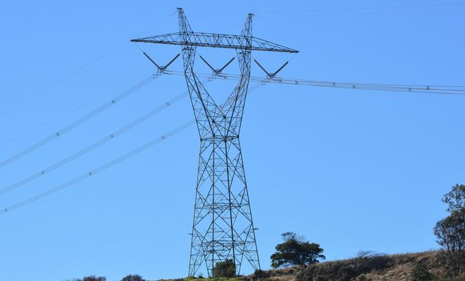 Torre de alta tensión de estructura metálica con cables eléctricos bajo un cielo despejado.