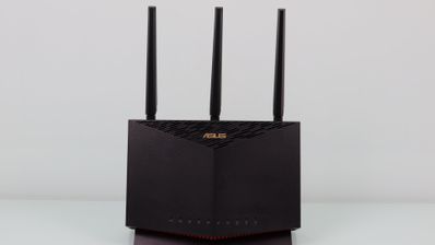 Router ASUS RT-AX86U en color negro con tres antenas externas verticales sobre una superficie blanca.