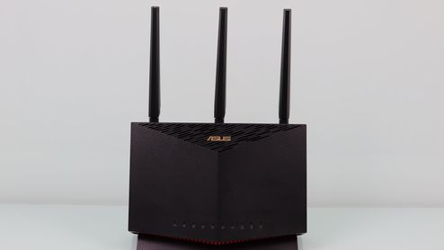 Router ASUS RT-AX86U en color negro con tres antenas externas verticales sobre una superficie blanca.