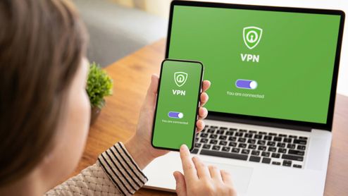 Usuario con un smartphone frente a un ordenador portátil, ambos mostrando una interfaz de conexión VPN activada sobre fondo verde.