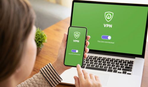 Usuario con un smartphone frente a un ordenador portátil, ambos mostrando una interfaz de conexión VPN activada sobre fondo verde.