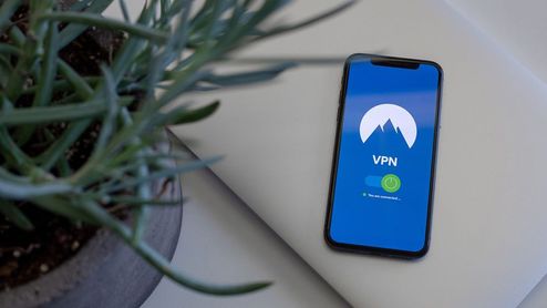 Teléfono móvil mostrando una aplicación de VPN activada junto a una planta y un portátil.